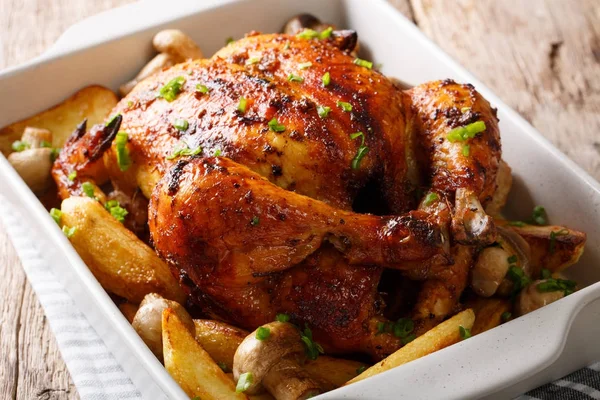 Whole baked chicken with mushrooms and potatoes close-up in a ba