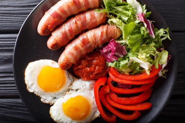 Fried sausages wrapped in bacon, eggs and fresh salad close-up. — Stock Photo, Image