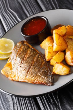 Kızarmış Dorado filetosu, patatesli ve soslu yakın plan bir tabakta.