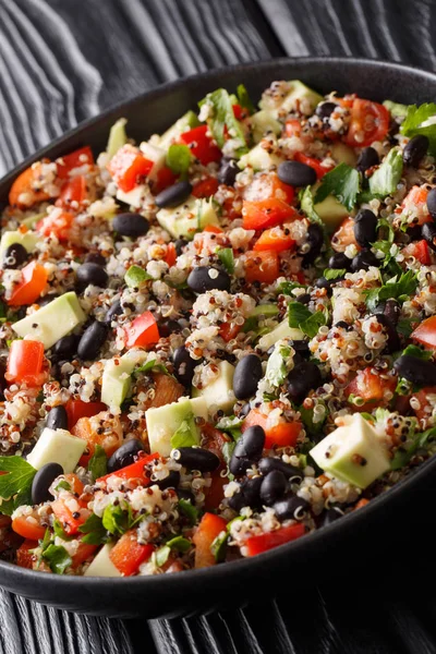 Mexican salad of quinoa, avocado, peppers, tomatoes and black beans close-up in a plate on the table. vertica