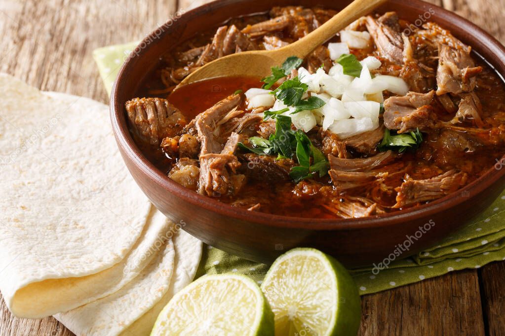Mexican style slow cooked beef stew Birria de Res served with lime and tortilla closeup in a bowl on the table. horizonta