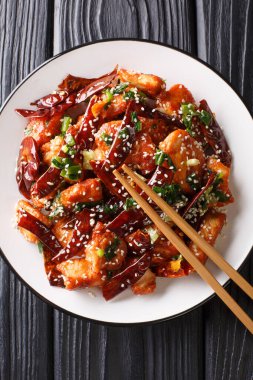 Crispy, tasty chicken pieces stir-fried with a generous amount of dried chillies and Sichuan pepper close-up in a plate on the table. Vertical top view from abov clipart
