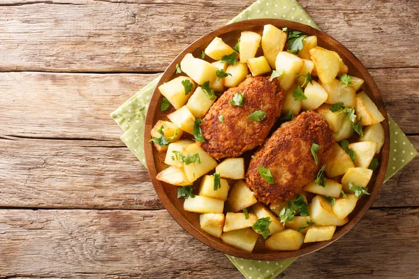 Traditional Russian cuisine pozharsky cutlets in breading with fried potatoes close-up in a plate on the table. Horizontal top view from abov