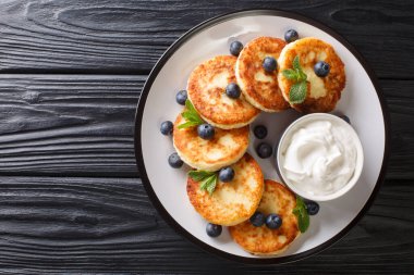 Ukrayna kahvaltısı süzme peynirli krep, yaban mersini, nane ve ekşi krema, masada yakın plan. Yukarıdan yatay üst görünüm