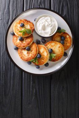 Süzme peynir şurubundan yapılmış sağlıklı bir kahvaltı. Masanın üzerinde yabanmersini, nane ve ekşi krema var. yukarıdan dikey üst görünüm