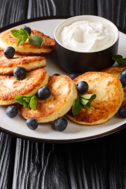 Süzme peynir şurubundan yapılmış sağlıklı bir kahvaltı. Masanın üzerinde yabanmersini, nane ve ekşi krema var. dikey