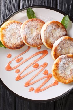 Syrniki, pudra şekeri ve böğürtlen reçelini masaya yakın bir tabakta servis ediyor. Yukarıdan dikey üst görünüm