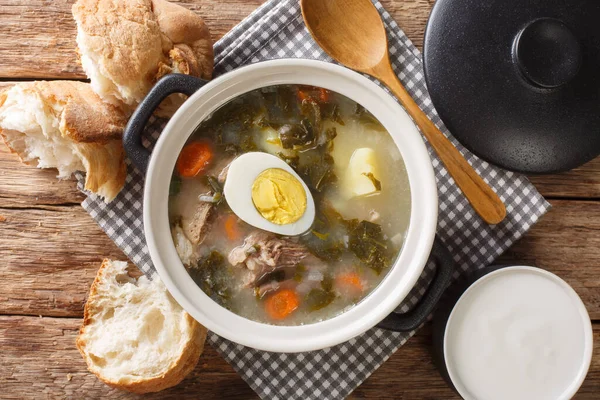 Green borsch of sorrel, vegetables, eggs with meat in a saucepan served with bread and sour cream close-up on the table. Horizontal top view from abov — Stock Image Green Borsch Sorrel Vegetables Eggs Meat Saucepan Served Bread Sour Royalty Free Stock Photos
