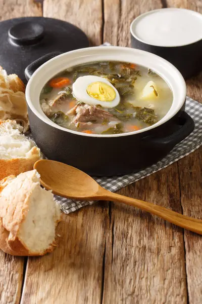 Hot light green borsch of sorrel, vegetables, eggs with meat served with bread and sour cream close-up on the table. vertica — Stock Image Hot Light Green Borsch Sorrel Vegetables Eggs Meat Served Bread Stock Picture