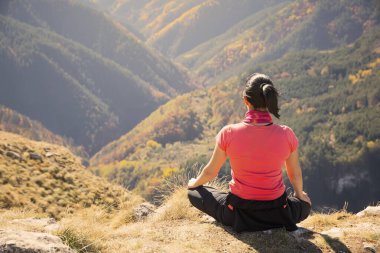 Lotus 'ta oturan genç, güzel yogacı kadın kayanın ucunda poz veriyor. Panoramik sonbahar dağ manzarası.