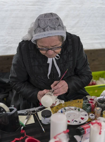 An elderly woman in traditional costume is busy painting candles — Stock Photo, Image