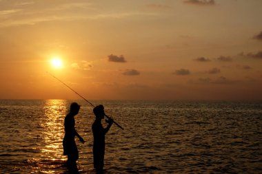 Gün batımı kumsalında eğlenen bir sürü insan.