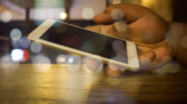 Akıllı telefonu ahşap masada tutarken arka planda bokeh ışıklandırma vardı. 