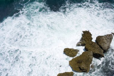 Dalgalar kayalıklara çarpıyor, yukarıdan görünüyor.