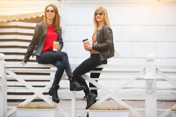 Portret van twee mooie jonge vriendinnen met papieren kopjes koffie in handen. — Stockfoto