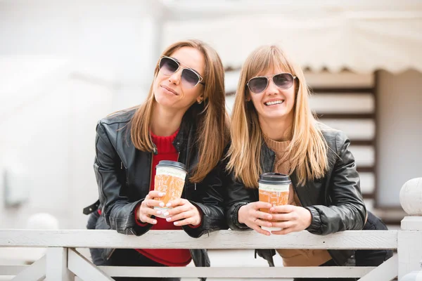 Portrait of two beautiful young girlfriends with paper cups of coffee in hands. — Stock Photo, Image