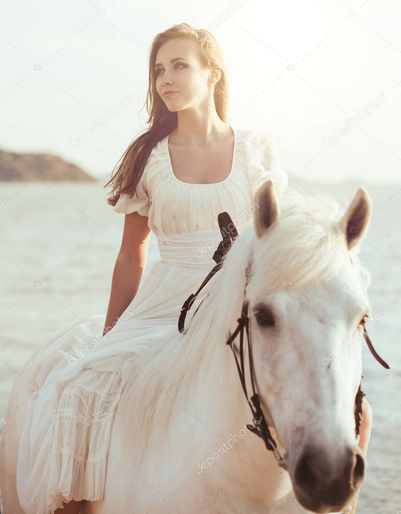 Girl in white dress with horse on the beach