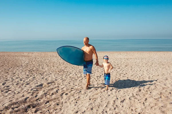 Surfer and his son are going to surf in the ocean in a sunny day — Stock Photo, Image