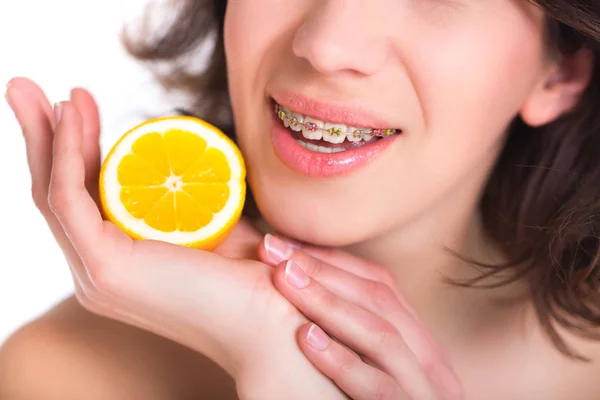 Hermosa chica con la piel perfecta y frenos multicolores posando con limón en la palma —  Fotos de Stock