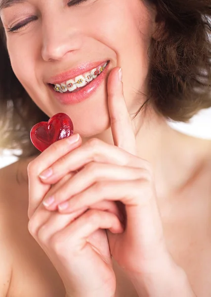 Hermosa chica con la piel perfecta y frenos multicolores posando con el corazón pequeño en las manos —  Fotos de Stock