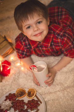 Çikolata meşrubatını ile Noel ağacı altında döşeme çocuk.