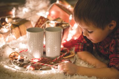 Çikolata meşrubatını ile Noel ağacı altında döşeme çocuk.