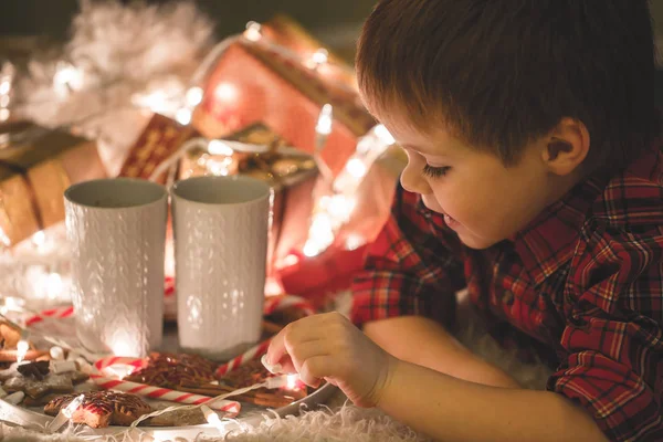 Boy laying under christmas tree with chocolate drink. — Stock Photo, Image