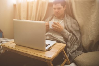 Genç adam Bad dizüstü bilgisayar ve çay döşeme.