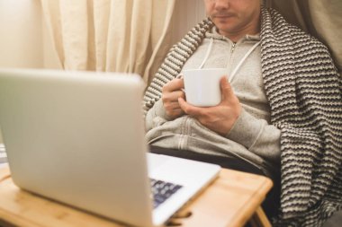 Genç adam Bad dizüstü bilgisayar ve çay döşeme.