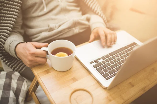 Young man laying in bad with laptop and cup of tea. — Stock Photo, Image