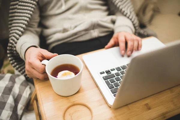 Jeune homme couché dans le mauvais avec ordinateur portable et tasse de thé . — Photo