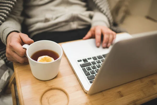 Jeune homme couché dans le mauvais avec ordinateur portable et tasse de thé . — Photo