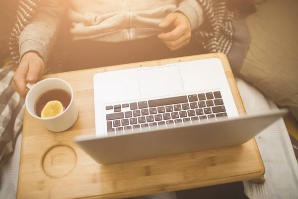 Jeune homme couché dans le mauvais avec ordinateur portable et tasse de thé . — Photo