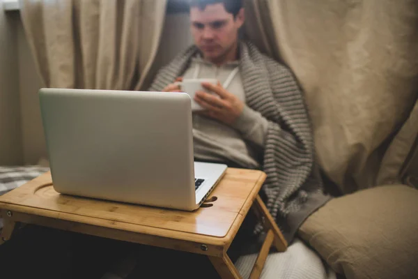 Young man laying in bad with laptop and cup of tea. — Stock Photo, Image