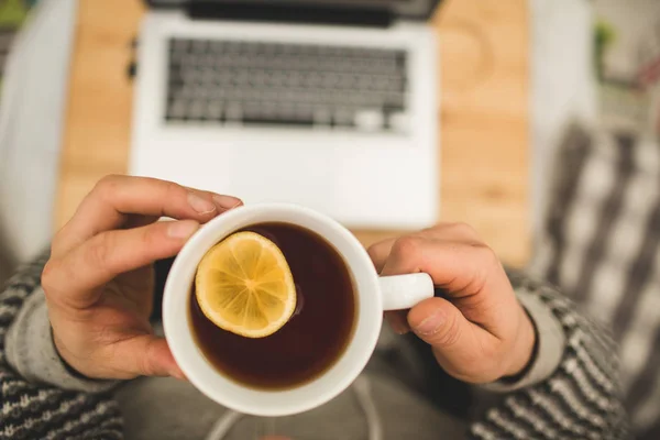 Top vue mains avec tasse de thé au citron et ordinateur portable — Photo