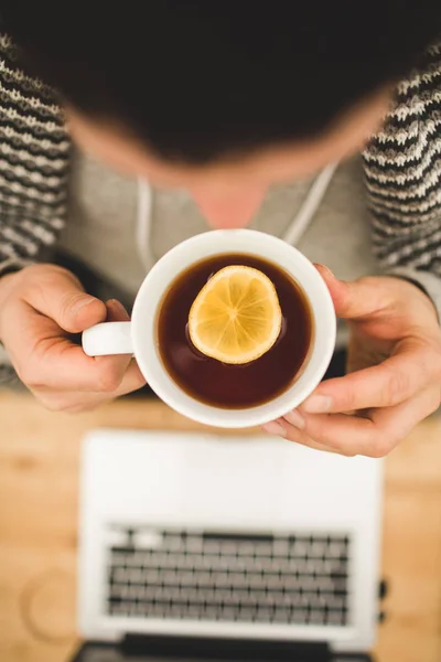 Hände von oben mit einer Tasse Tee mit Zitrone und Laptop — Stockfoto