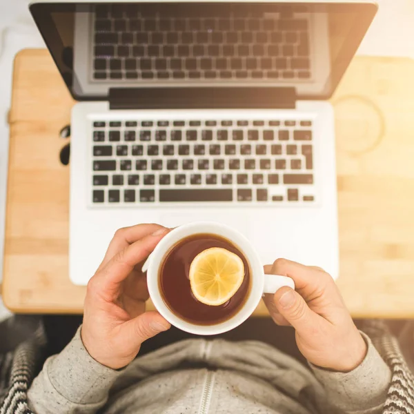 Top view hands with cup of tea with lemon and laptop — Stock Photo, Image