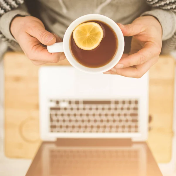 Bovenaanzicht handen met kopje thee met citroen en laptop — Stockfoto