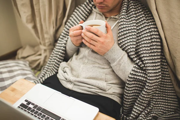 Young man laying in bad with laptop and cup of tea. — Stock Photo, Image