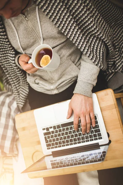 Jeune homme couché dans le mauvais avec ordinateur portable et tasse de thé . — Photo