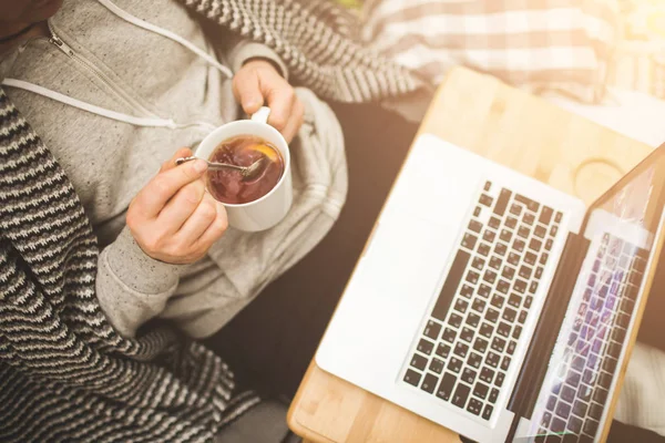 Jeune homme couché dans le mauvais avec ordinateur portable et tasse de thé . — Photo