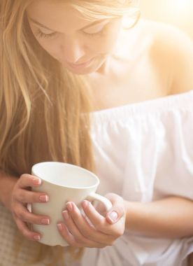 Güzel genç gülümseyen kadın kahve zamanında tadını çıkarırken oturma odasında kanepede rahatlatıcı.