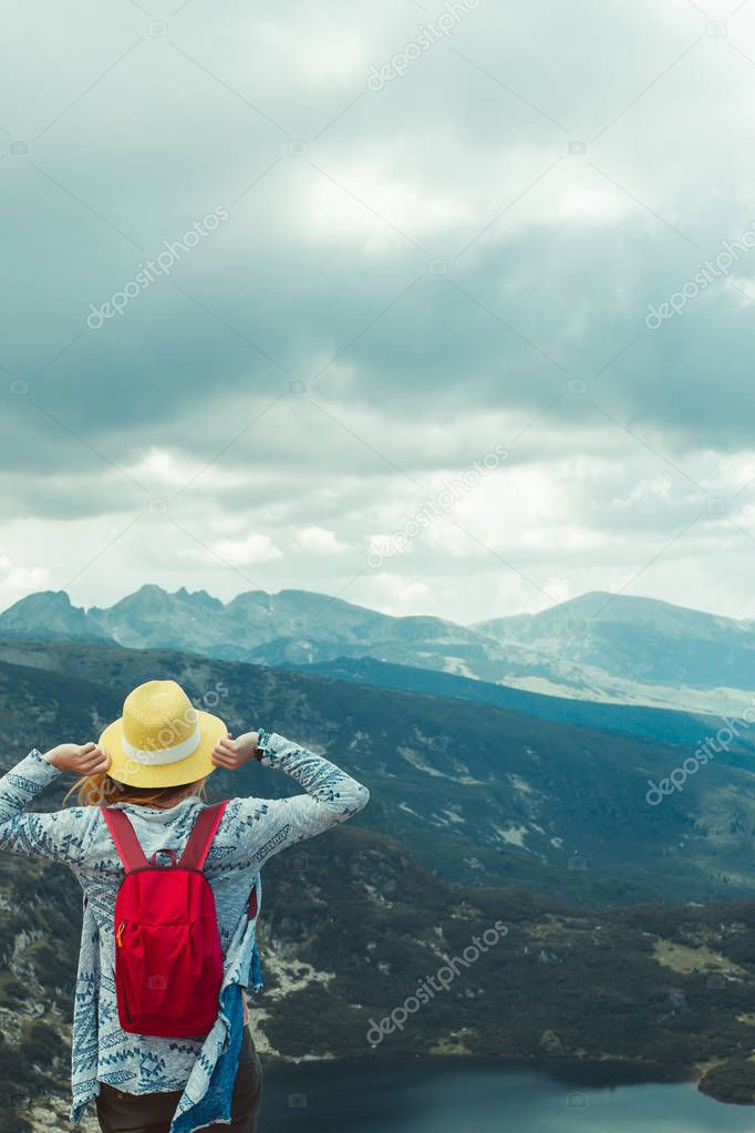 Young woman hiking in Rila mountains, Bulgaria. woman is holding her hat. strong wind. back view. Great view to the lake