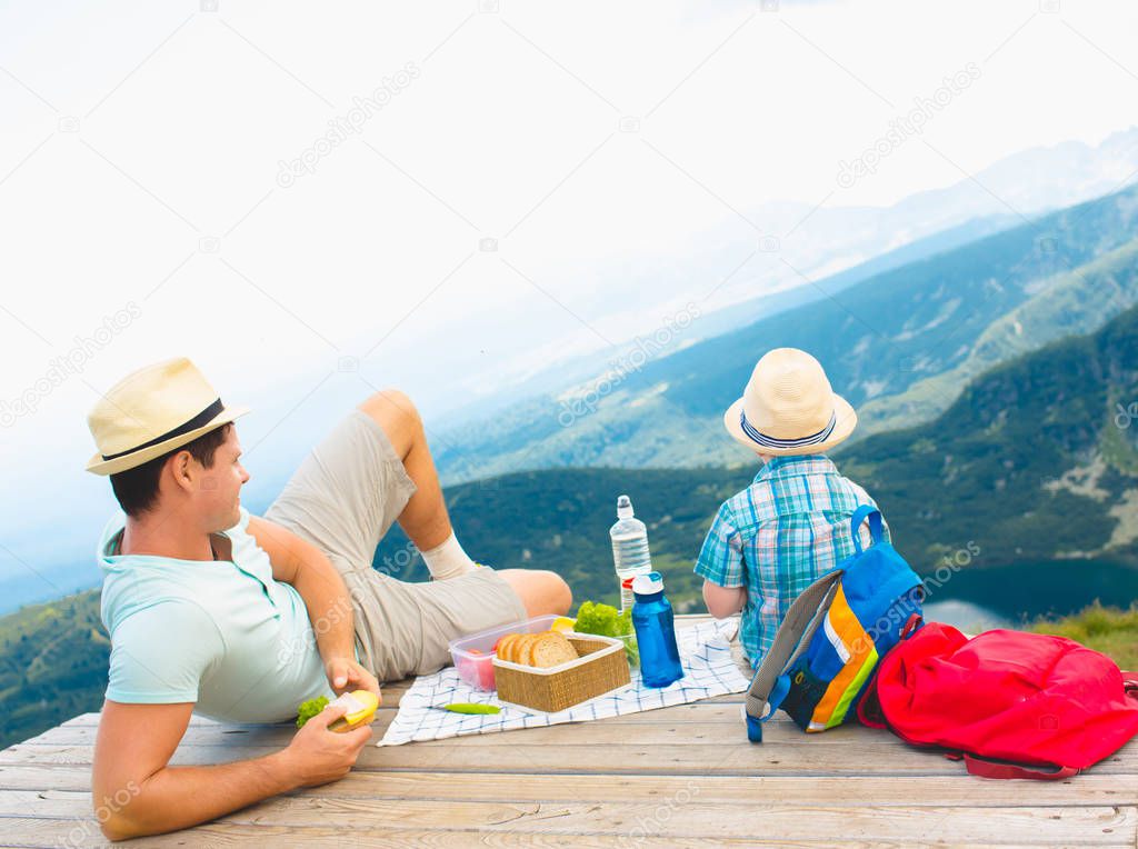 Father and son eat healthy sandwiches on a picnic in the mountains. Rila Lakes in Bulgaria. back view