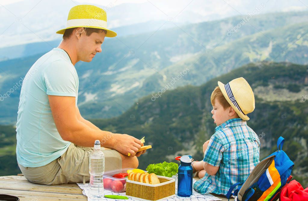 Father and son eat healthy sandwiches on a picnic in the mountains. Rila Lakes in Bulgaria.
