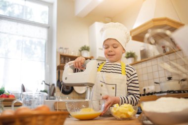 Aşçı şapkalı küçük çocuk yemek yapıyor.