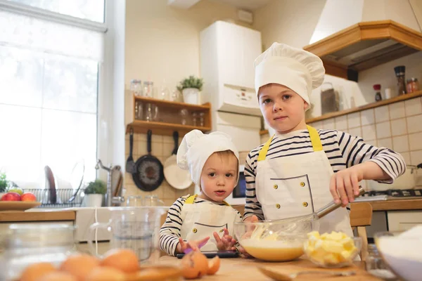 Dois irmãozinhos de chapéu de chef estão cozinhando — Fotografia de Stock