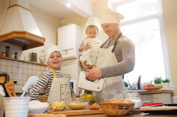 O pai e os filhos nos chapéus do chef estão a cozinhar. — Fotografia de Stock