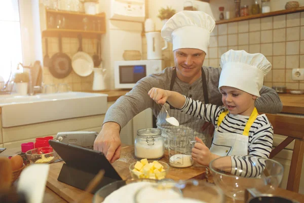 Pai e filho em chapéus de chef estão cozinhando — Fotografia de Stock