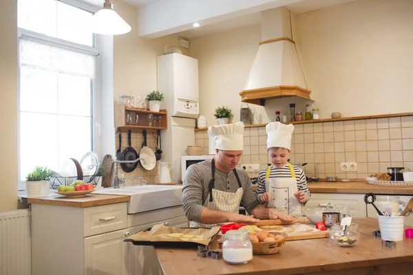 Pai e filho em chapéus de chefs estão cozinhando — Fotografia de Stock